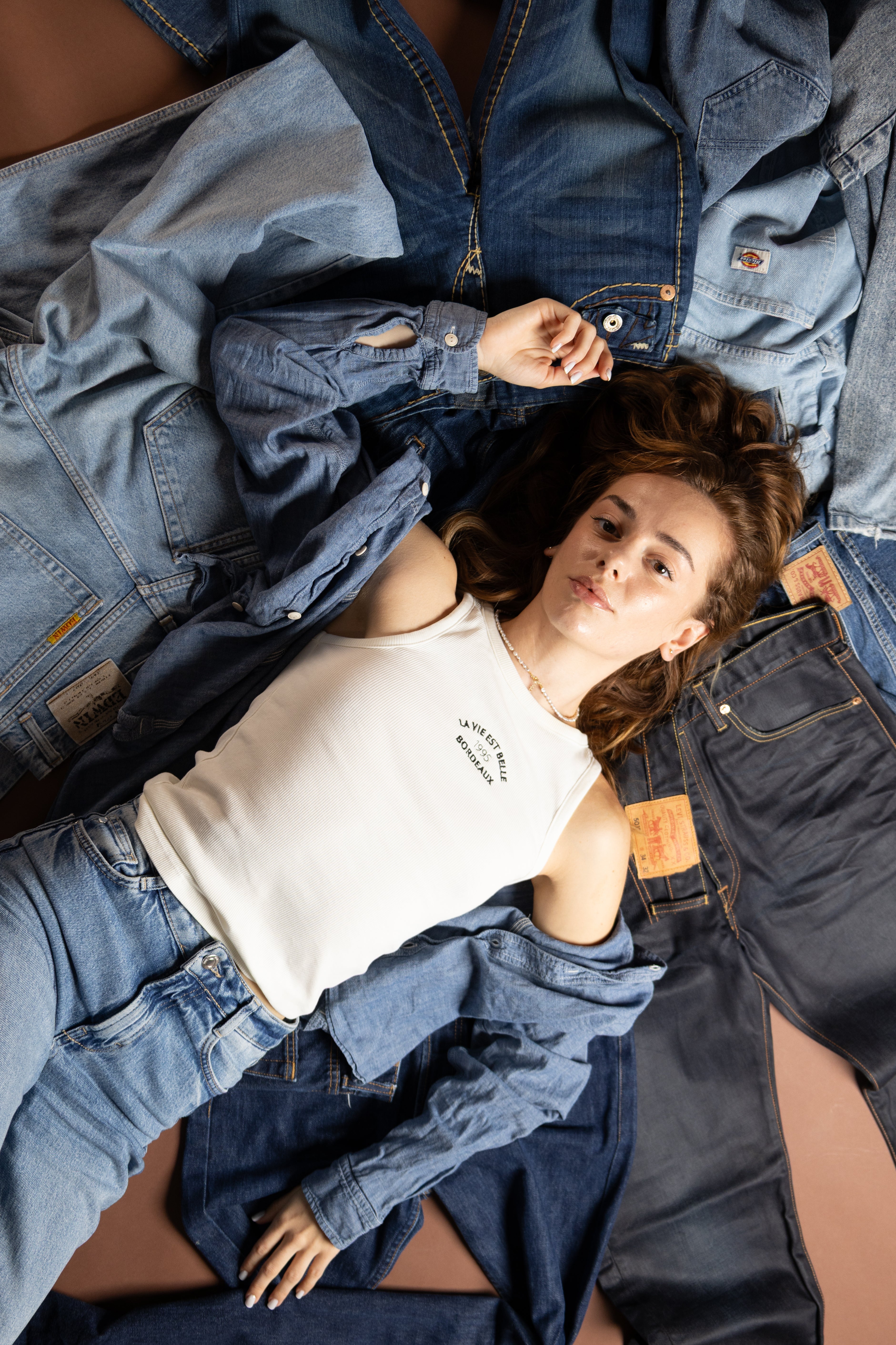 Woman lying among denim clothing with a neutral background